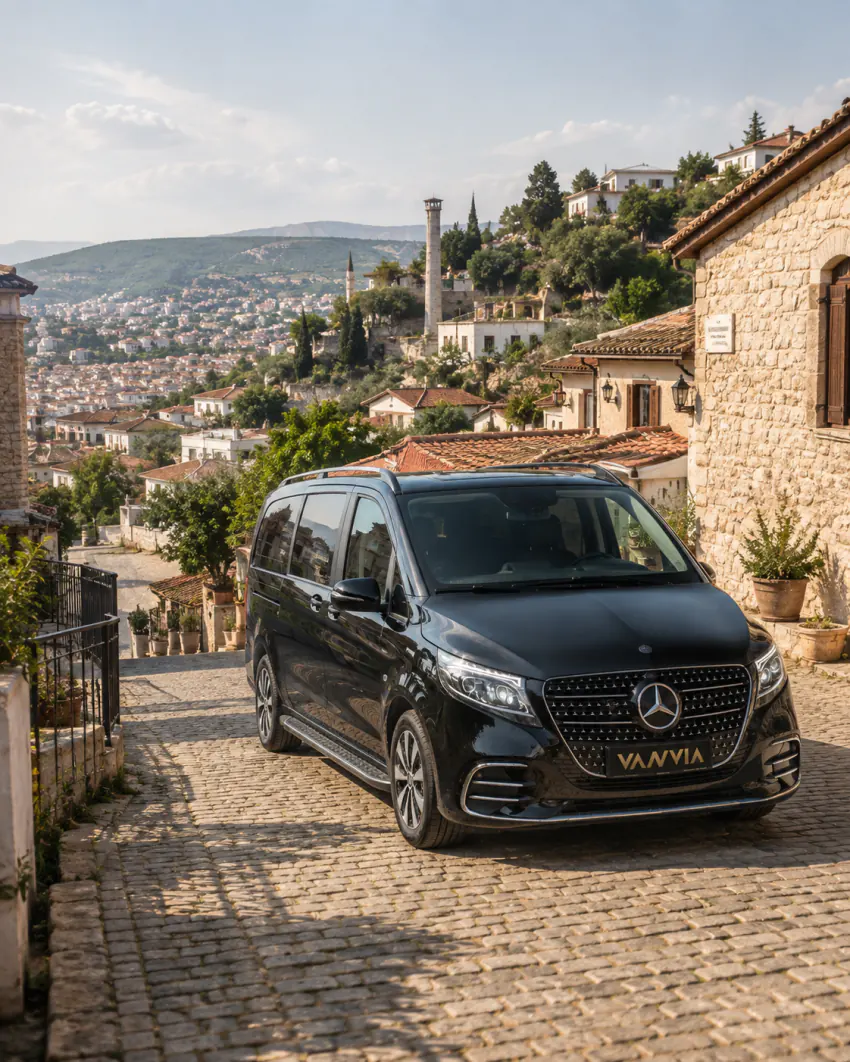 The Vanvia vehicle passing through a red-roofed, cobblestone street in a historic Aegean hillside town