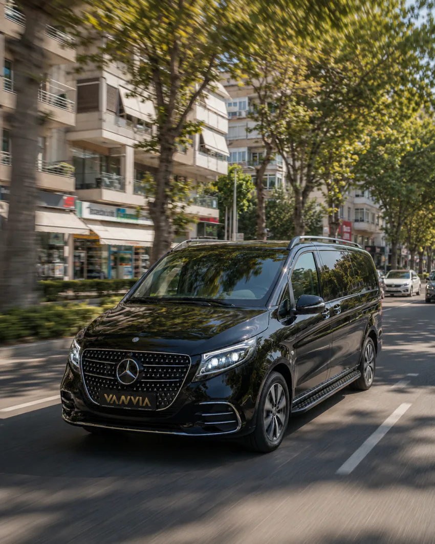 A black Vanvia VIP vehicle driving along a tree-lined urban street with shopfronts