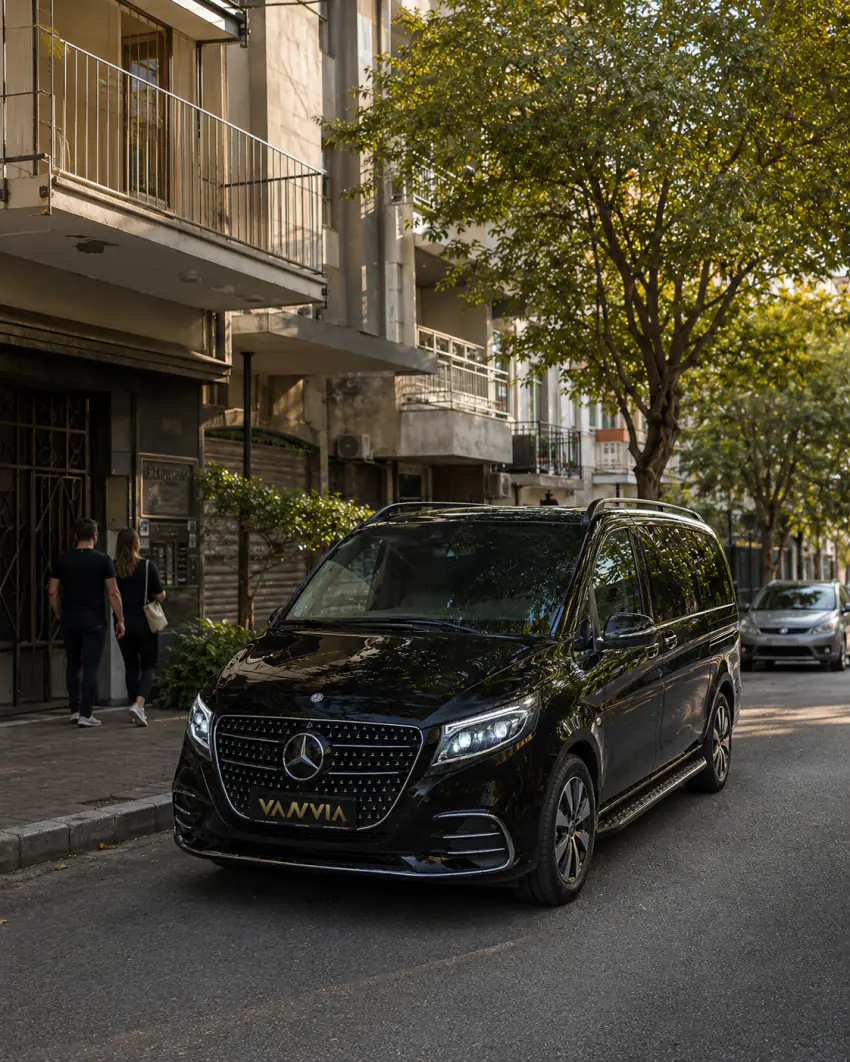 A black Vanvia VIP vehicle parked on a neighbourhood street with apartment buildings, with two pedestrians visible walking nearby