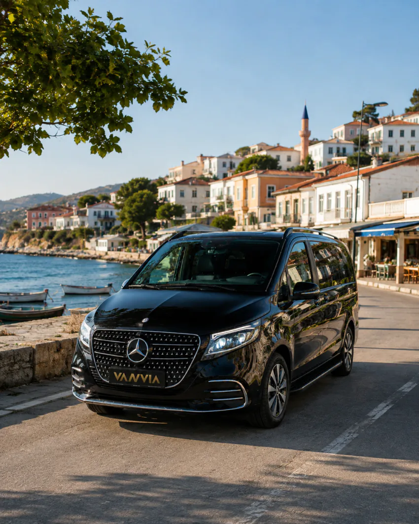 A black Vanvia VIP vehicle parked along a coastal-town promenade, with a few small boats and a minaret visible nearby