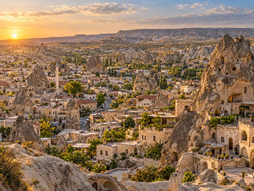 Göreme'nin cave-hotel bölgesinin yükseklikten görünümü; peri bacalarının içine ve çevresine inşa edilmiş taş yapılar, teraslar ve bir minare, gün ışığında; araç görünmüyor
