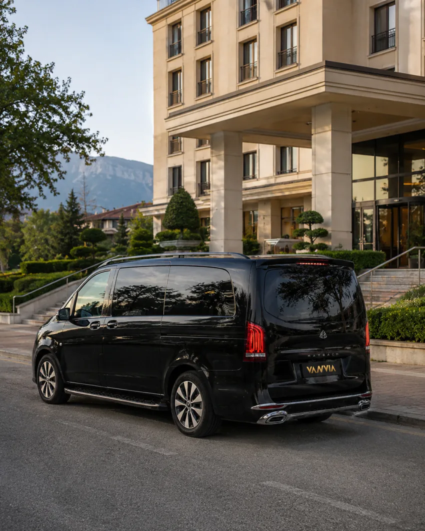 Rückansicht eines schwarzen Vanvia-VIP-Transferfahrzeugs, das vor einem Hotelgebäude mit Bergen im Hintergrund steht