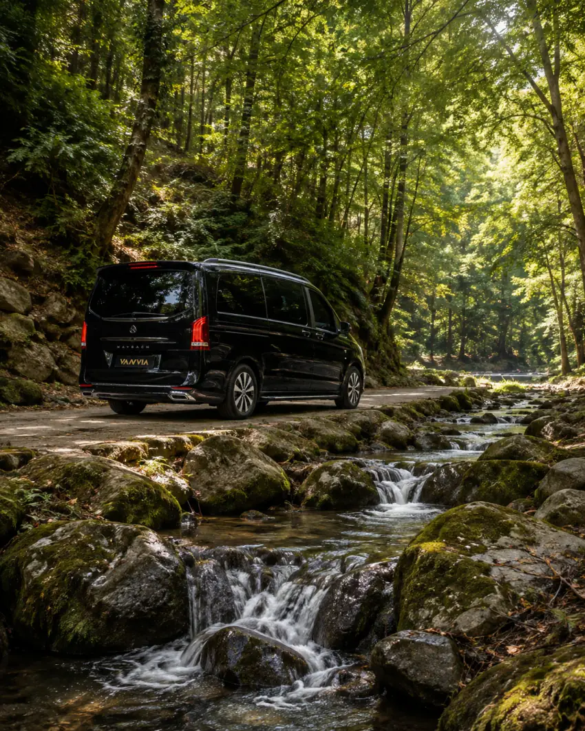 Rückansicht eines schwarzen Vanvia-VIP-Transferfahrzeugs, das neben einem Waldbach steht