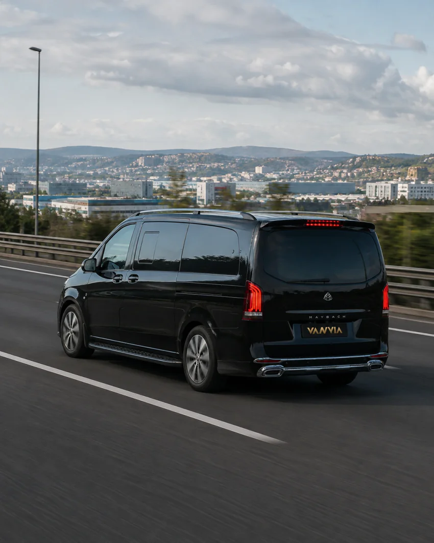 Rückansicht eines schwarzen Vanvia-VIP-Transferfahrzeugs bei der Fahrt auf einer Autobahn, in der Ferne eine Stadtsilhouette auf einem Hügel