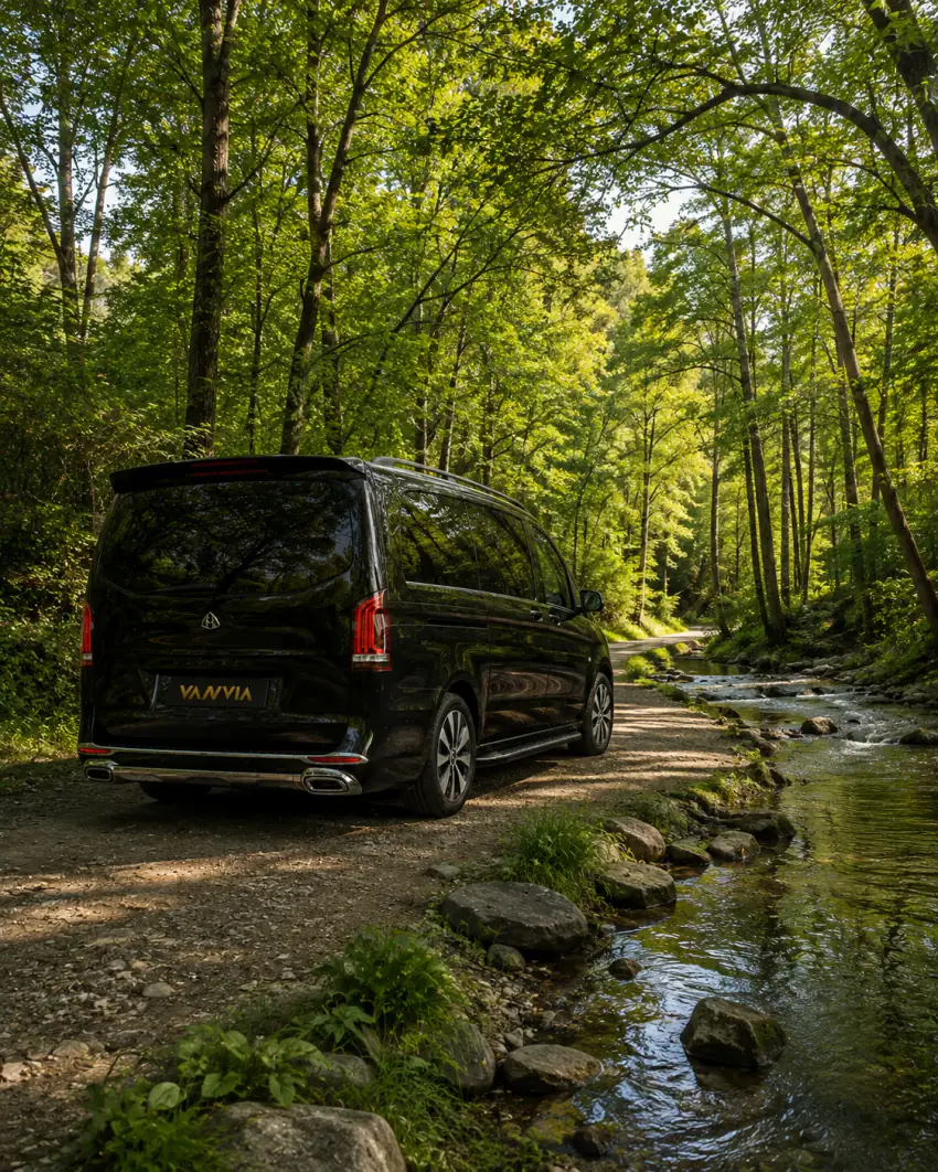 Rückansicht eines schwarzen Vanvia-VIP-Transferfahrzeugs, das auf einem Feldweg neben einem steinigen Waldbach steht