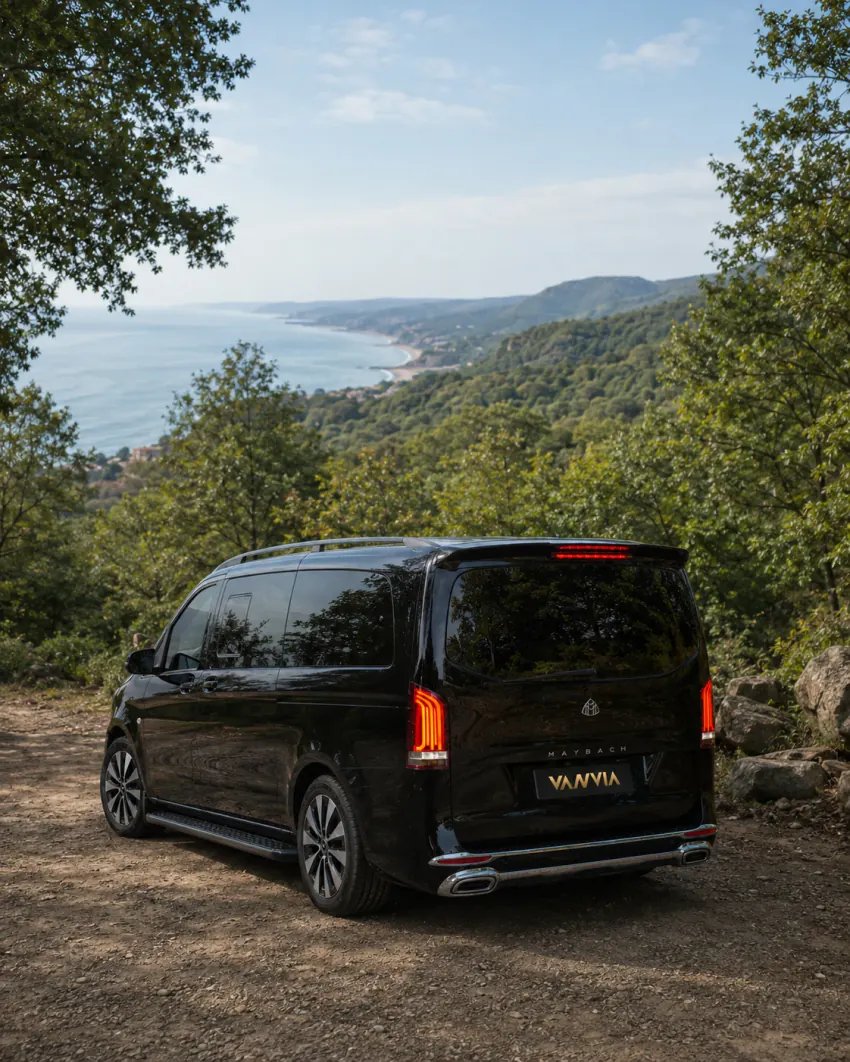 Schräge Rückansicht eines schwarzen Vanvia-VIP-Transferfahrzeugs, das auf einem Waldweg mit Blick auf die Schwarzmeerküste steht