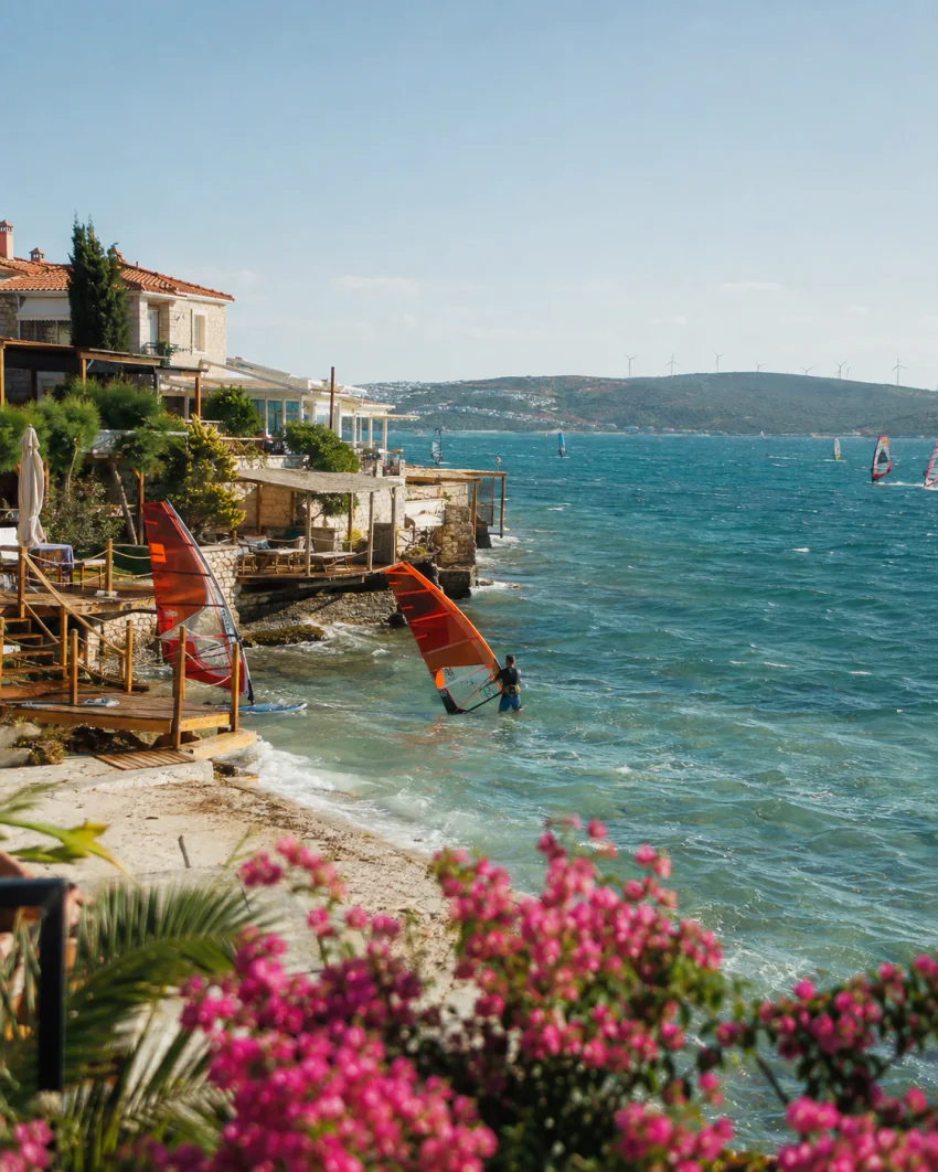 Ein Windsurfer auf türkisfarbenem Wasser vor dem Hafen von Alaçatı