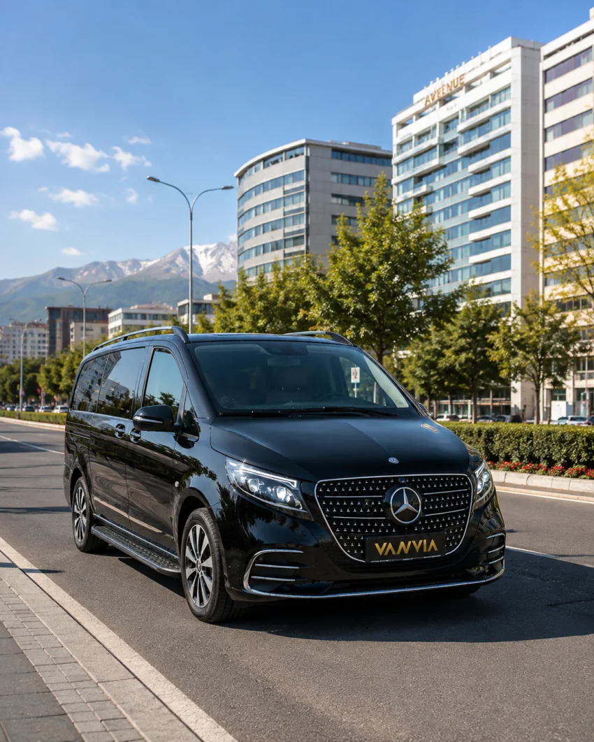 Kayseri'nin iş merkezindeki modern gökdelenlerin bulunduğu bir caddede ilerleyen siyah Vanvia VIP transfer aracı, gündüz açık gökyüzü altında