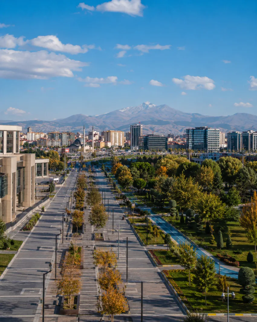 Kayseri'de geniş bir bulvarın gündüz, hiçbir araç olmadan çekilmiş görünümü; arka planda şehir binaları ve uzakta karla kaplı bir dağ silueti seçiliyor