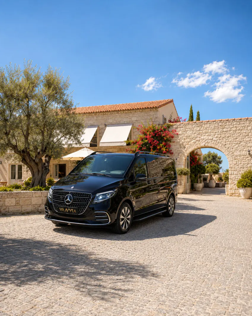 A black Vanvia vehicle waiting for a hotel transfer by day in a stone hotel courtyard with an olive tree