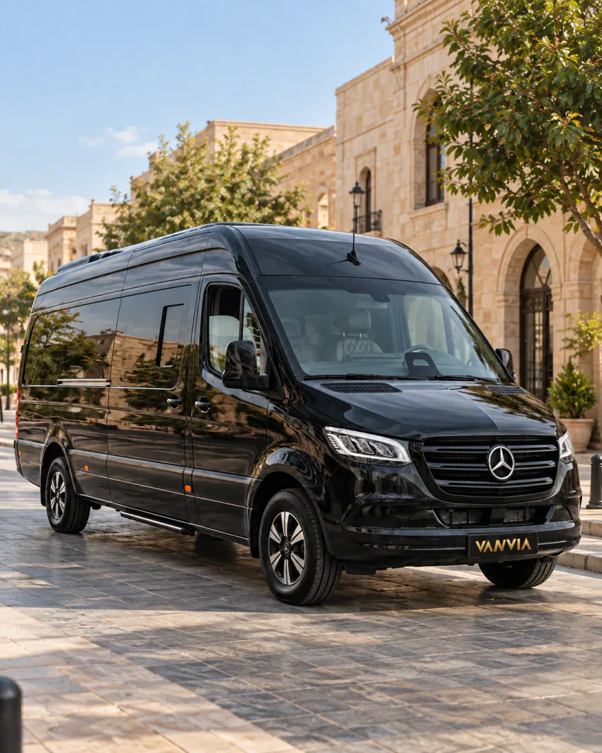 Bal rengi taş binaların önündeki taş döşeli bir alanda duran siyah Vanvia VIP transfer aracı