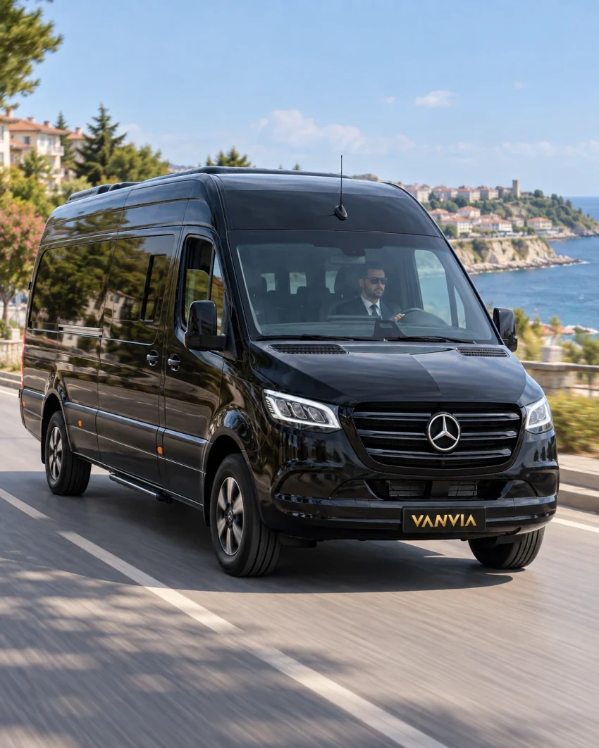Чёрный VIP-автомобиль Vanvia с водителем на прибрежной дороге, позади город на мысу